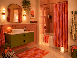 Full bathroom view with olive vanity, curved mirror, pink and orange shower curtain, wavy bath mat and warm lighting.